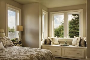 Bedroom with clear-glass casement windows above a window seat, with windows looking out on lush green foliage