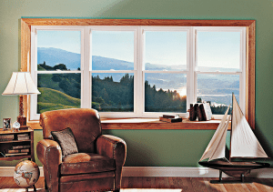 Four-unit bow window in sitting room behind easy chair with books on the shelf and an outdoor mountain view