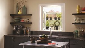 Interior view of a kitchen with a garden window looking out on another home and the shelf filled with potted plants