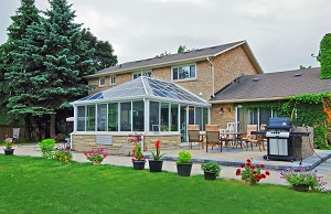 Rear view of a two-story house with side wing and lovely sunroom with matchng brick knee walls, outdoor table and chairs and grill on an adjacent slab